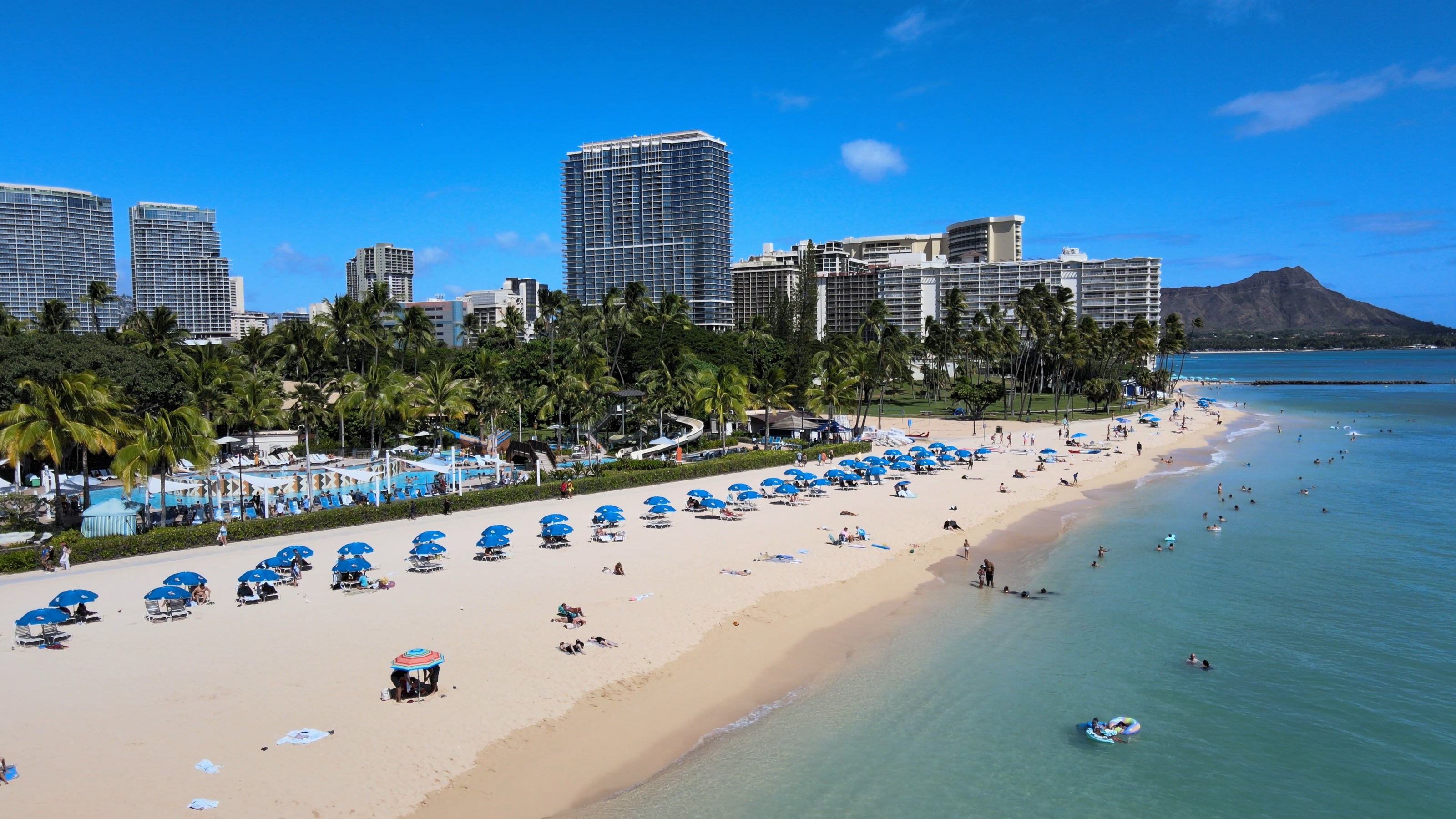 Stunning sunny beach photo of Waikiki Beach hotels and ocean.